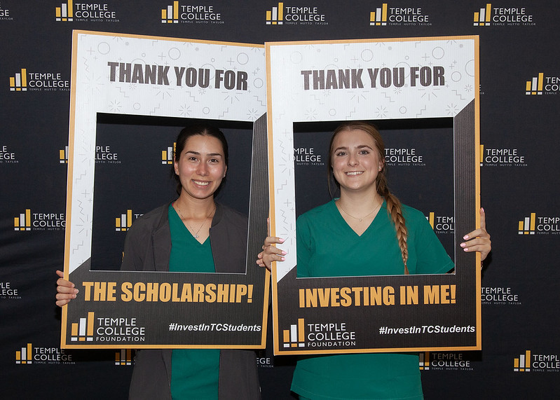 Two young female Nursing students in green scrubs pose with Thank you for the Scholarship signs